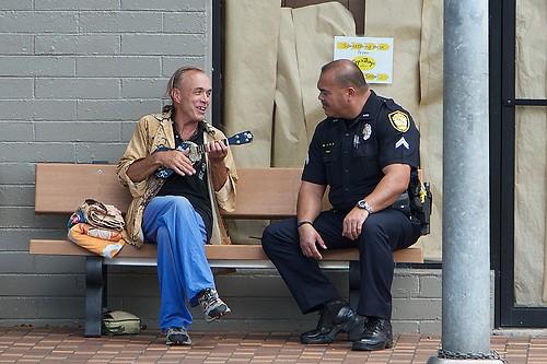 A police officer standing beside a street musician